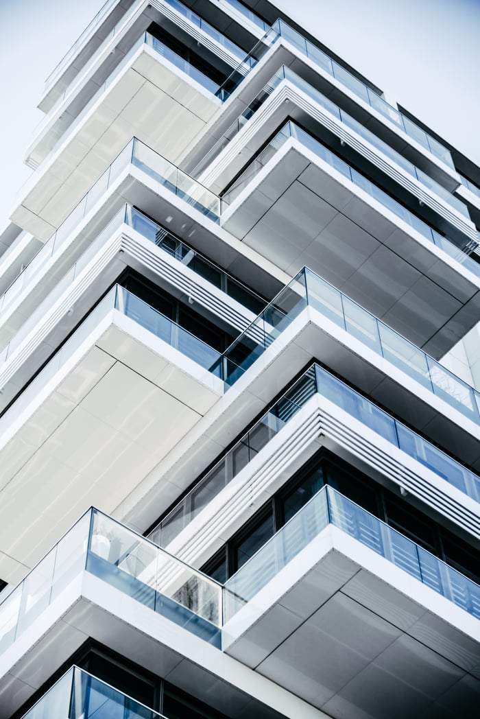 testimonials-img Close-up of a contemporary multi-layered building with glass balconies, showcasing modern architecture.